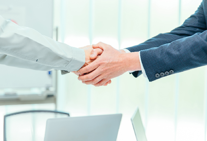 握手をする作業着の男性とスーツの男性の手。