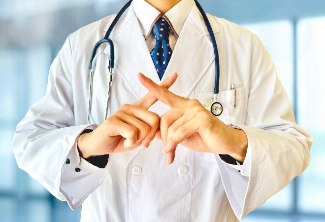 体の前で指でバツを作る白衣の男性。