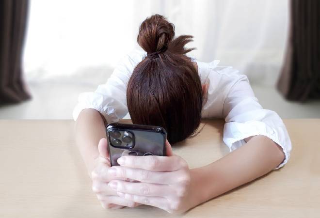 スマホを持ったまま机の上で突っ伏す女性。